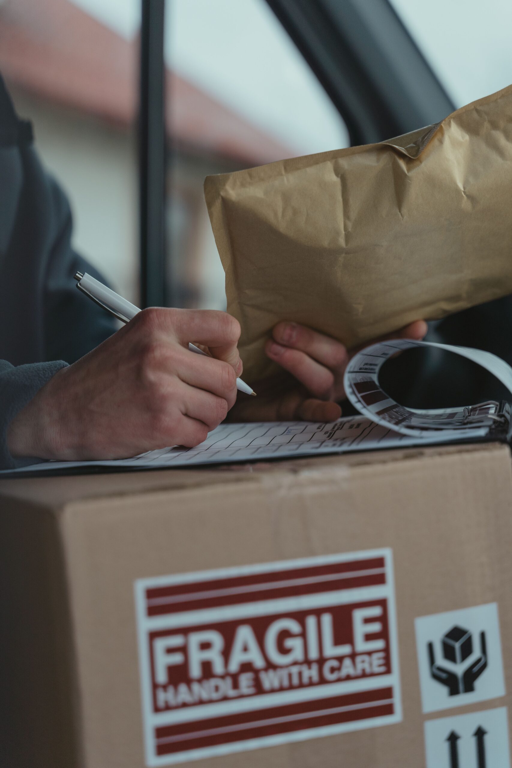 Close-up of a courier writing on a clipboard with a fragile package inside a vehicle.